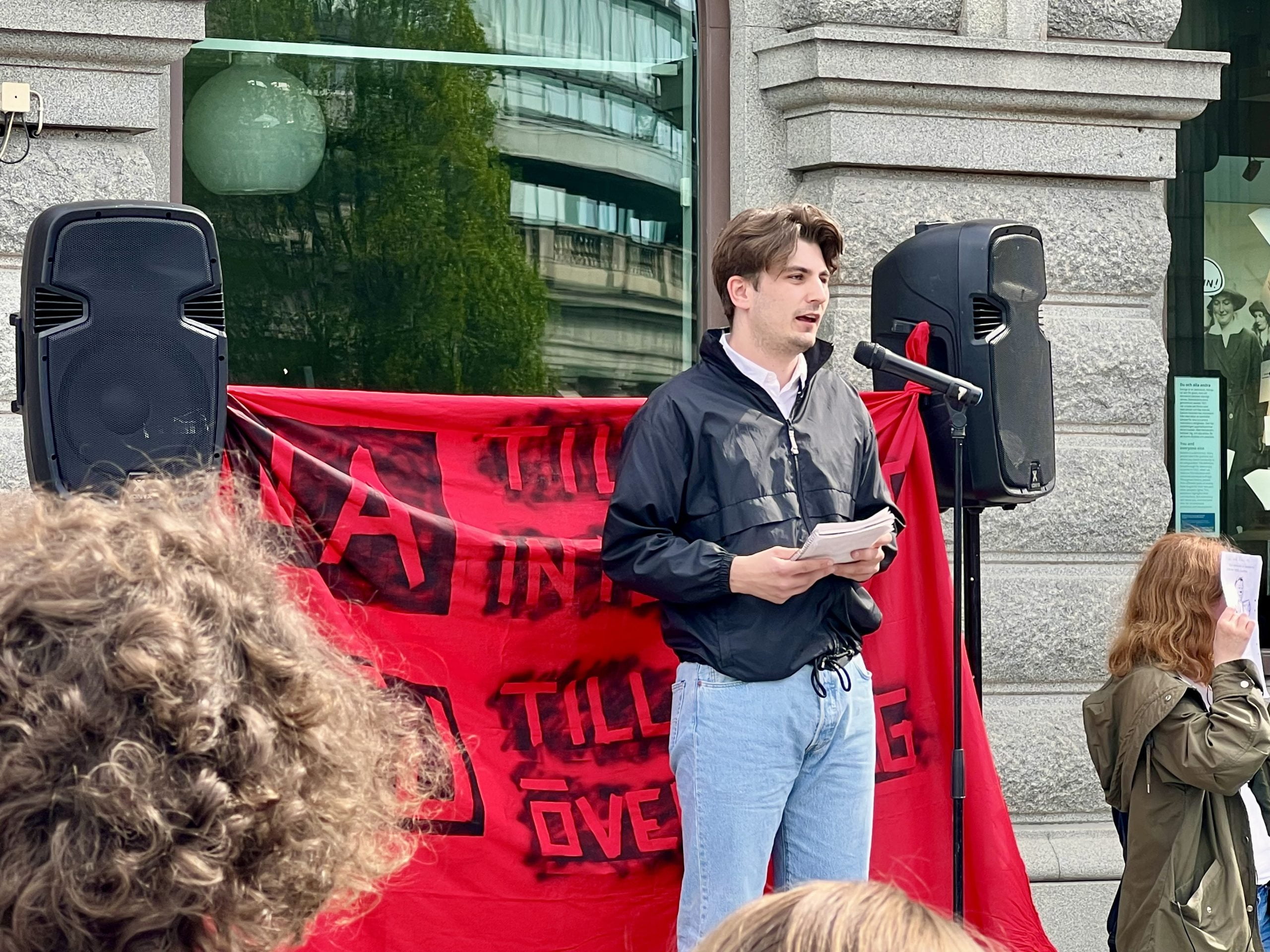 Anton Holmlund, vice ordförande för Liberala Ungdomsförbundet, talar vid demonstration. En banderoll med texten "ja till integritet, nej till övervakning” syns i bakgrunden.