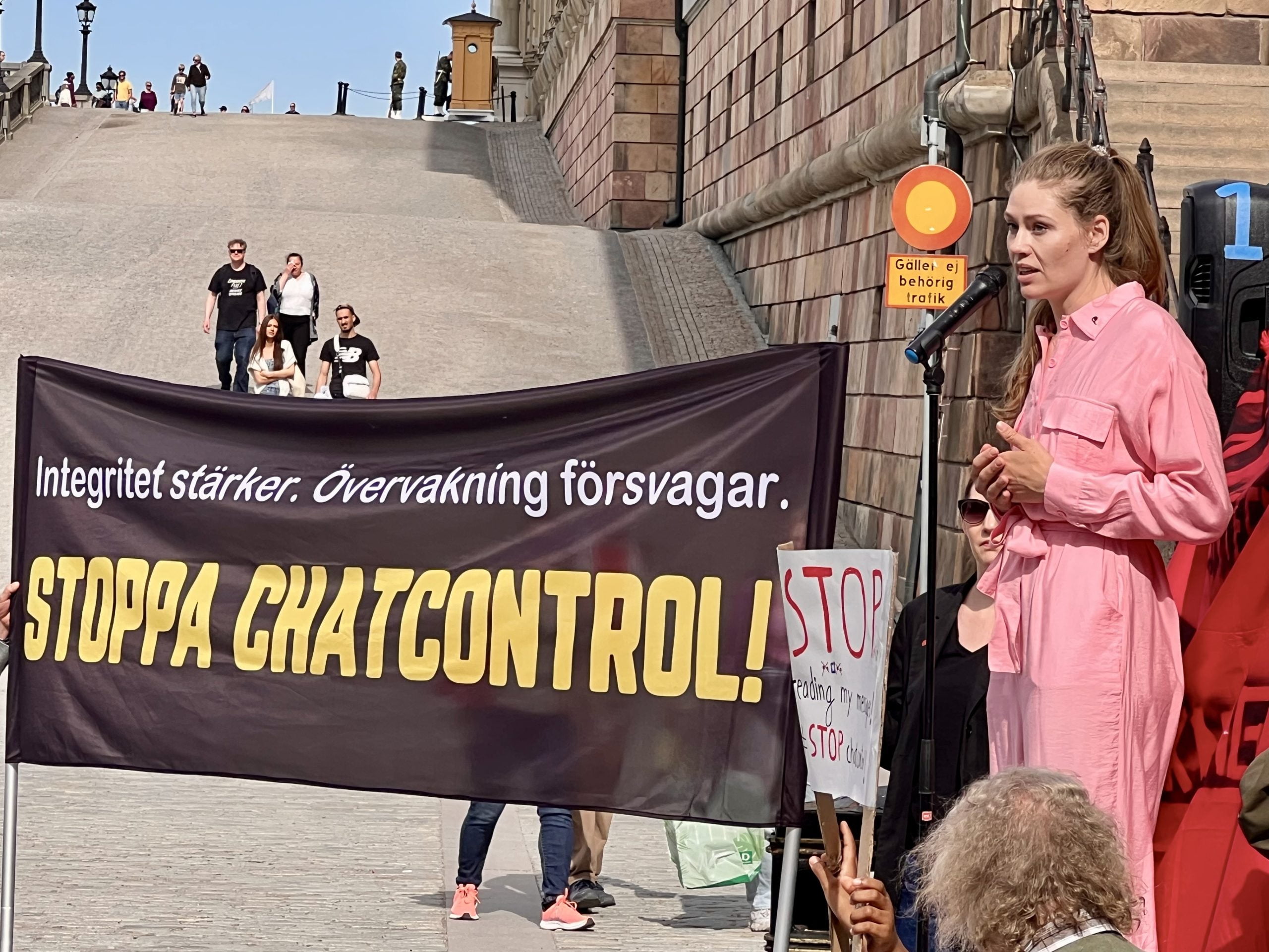 Katarina Stensson, partiledare för Piratpartiet, talar vid demonstration. En banderoll med texten ”integritet stärker, övervakning försvagar, stoppa Chat Control” syns i bakgrunden.