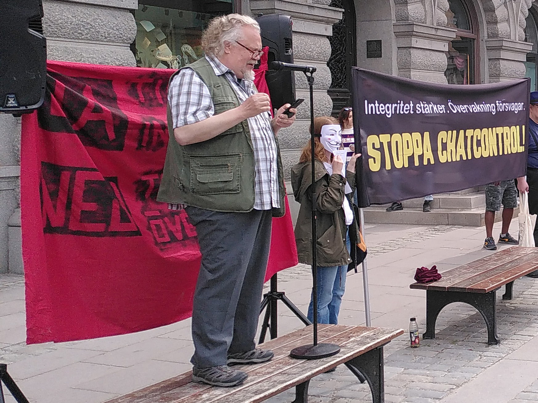 Henrik Alexandersson från 5 juli-stiftelsen talar vid demonstration. Banderoll med texterna "ja till integritet, nej till övervakning” och ”integritet stärker, övervakning försvagar, stoppa Chat Control” syns i bakgrunden.